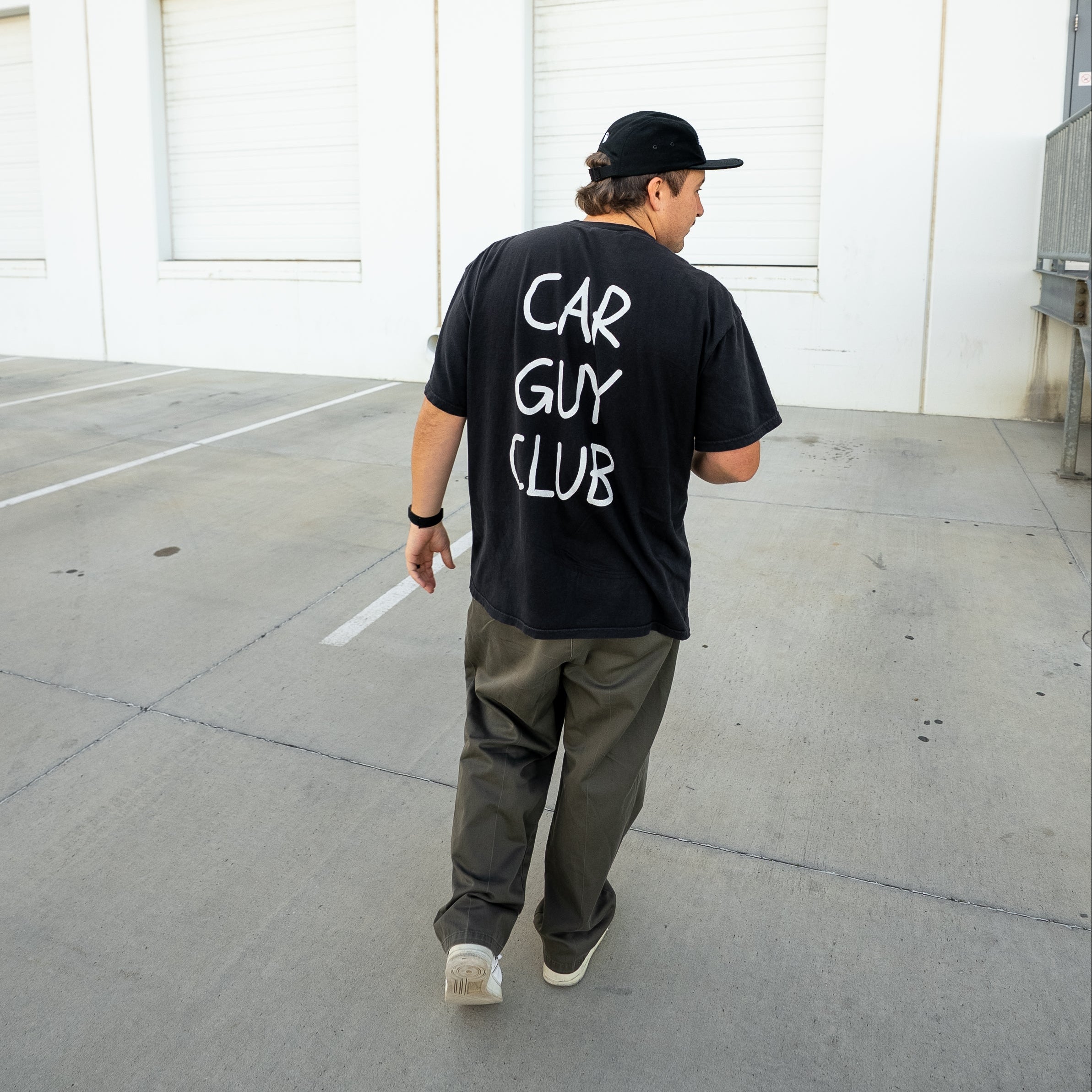 Person wearing a black 'Car Guy Club' t-shirt walking in an outdoor setting.