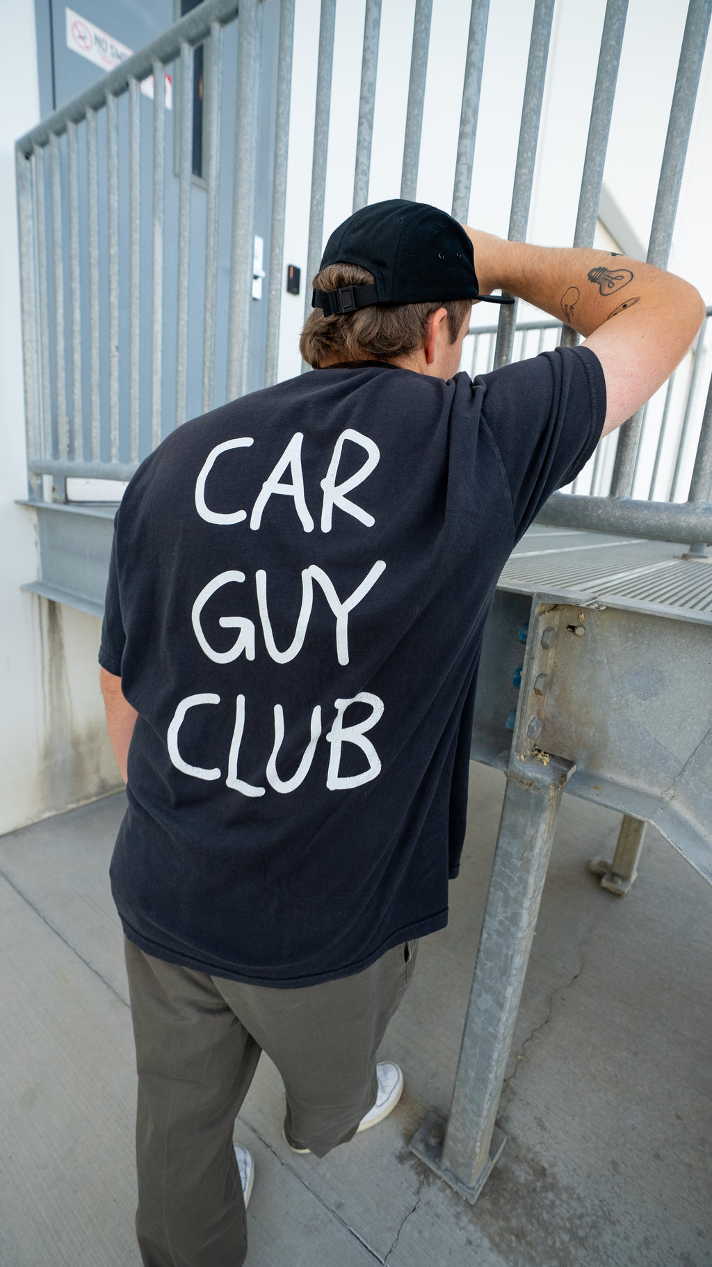 Person wearing a 'Car Guy Club' t-shirt standing on a balcony.