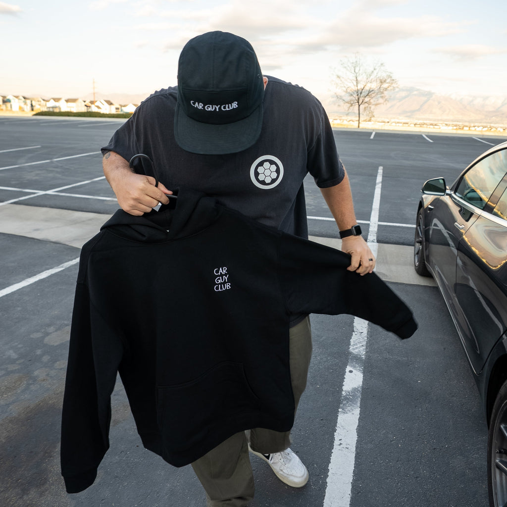 Person holding a black hoodie with a logo in a parking lot