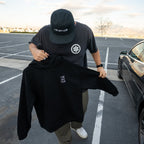 Person holding a black hoodie with a logo in a parking lot