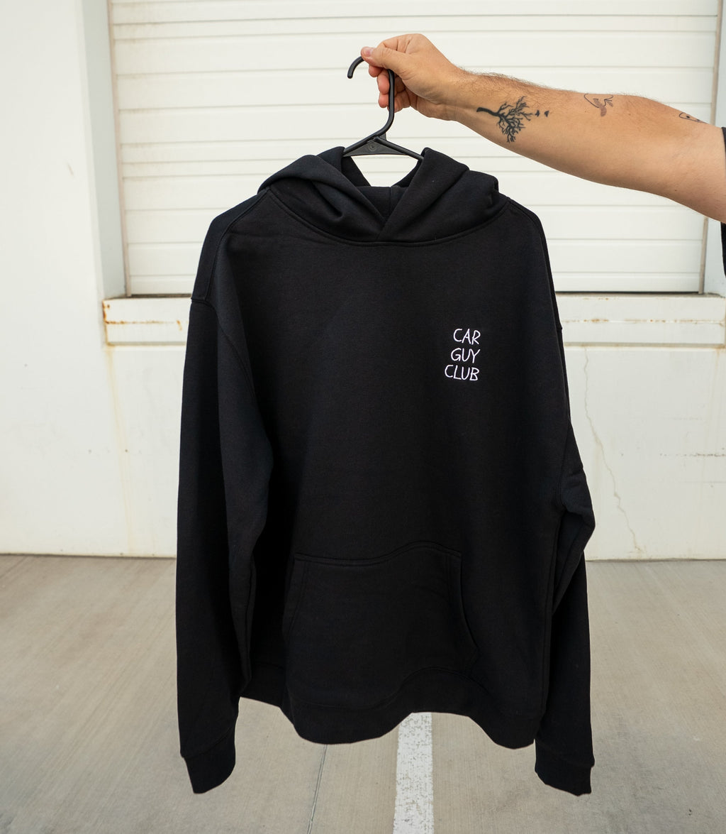 Black hoodie with text on a hanger against a white wall.