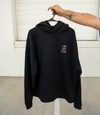 Black hoodie with text on a hanger against a white wall.