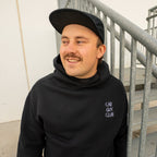 Man wearing a black hoodie with 'Car Guy Club' text, standing on a staircase.