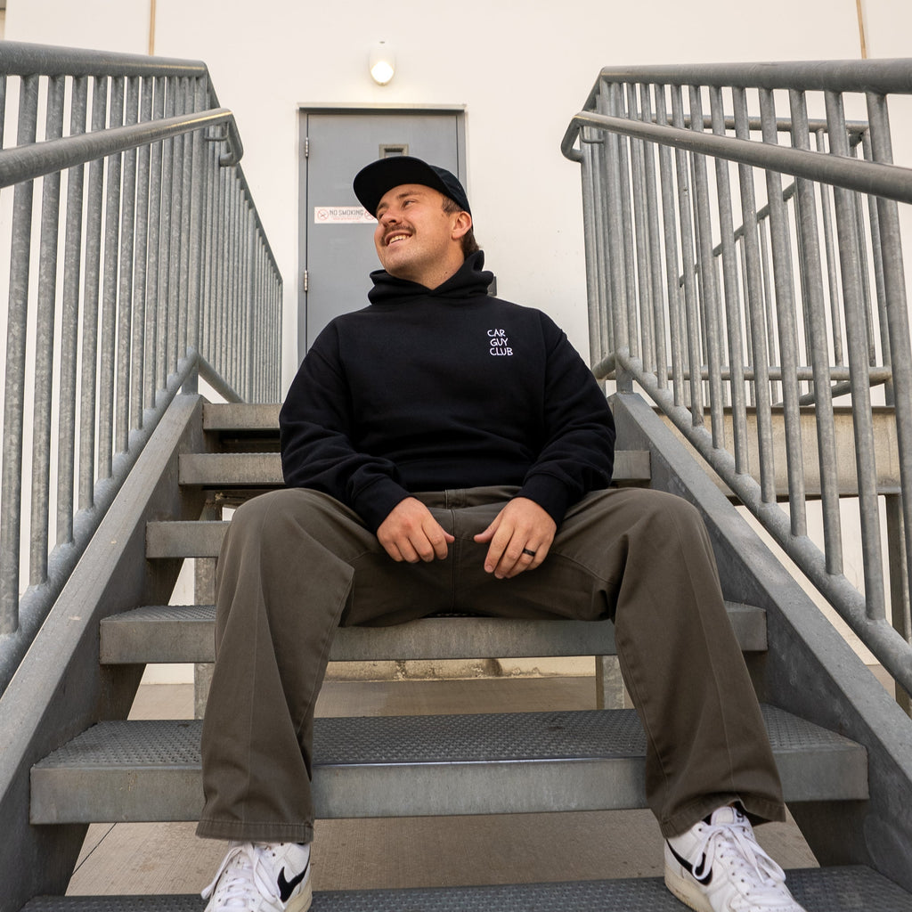 Person sitting on a set of stairs wearing a black hoodie, brown pants, and white sneakers.