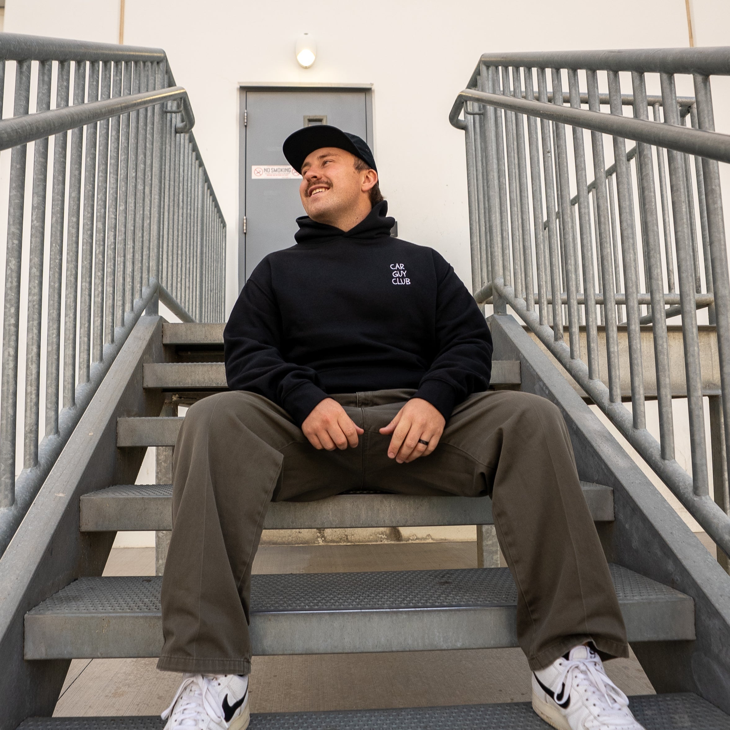 Person sitting on a set of stairs wearing a black hoodie, brown pants, and white sneakers.