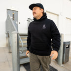 Man wearing a black hoodie with text and brown pants standing in an indoor setting.