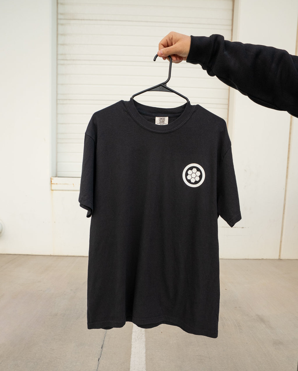 Black t-shirt with a white logo on a hanger against a plain background